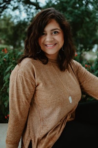 a smiling woman in a tan sweater sitting on a bench